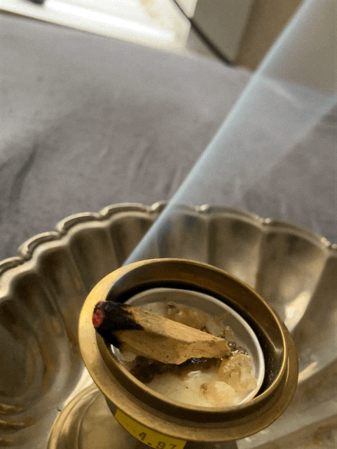 Close-up of a traditional incense burner with a stick of incense burning, producing smoke.