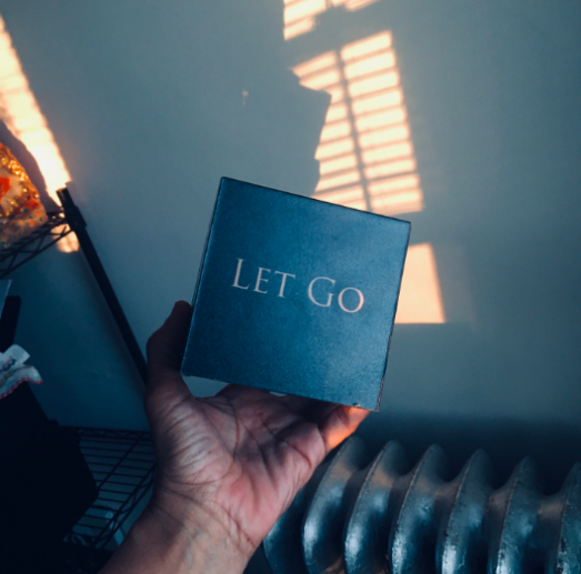 A black block with a light word on it, held up by a hand. The word says Let Go.